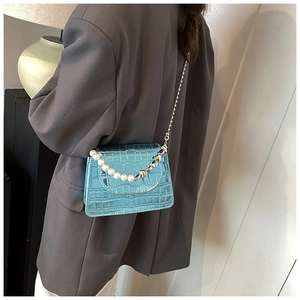 Détail du sac bleu clair à motif crocodile avec poignée en perles et chaîne argentée