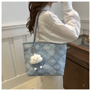 Quilted denim tote bag in light blue with cute white cloud charm shown on shoulder
