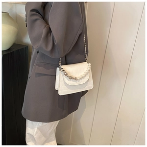 Détail d'un sac bandoulière blanc motif crocodile avec poignée en perles et chaîne
