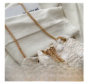 Detail of straw woven bucket bag with white floral embroidery and gold chain strap
