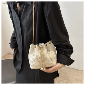 Detail of beige woven bucket bag featuring pearl drawstring and gold chain strap