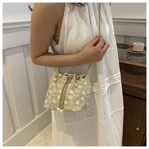 Close-up of straw bucket bag with white floral embroidery and gold chain strap