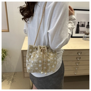 Detail of beige woven bucket bag with daisy embroidery, pearl drawstrings and chain