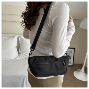Minimalist black nylon crossbody bag with adjustable wide strap shown on a casual model