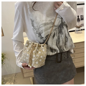 Straw bucket bag detail featuring floral lace embroidery and a delicate gold chain strap