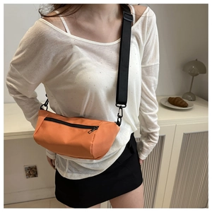 Detail of an orange nylon shoulder bag with black wide strap shown on a female model