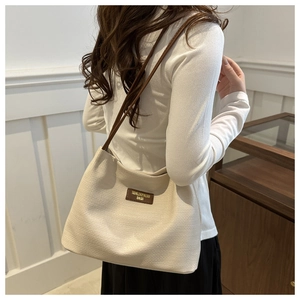 Close-up of woven cream tote bag with brown leather straps and branded patch detail