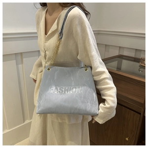 Detail of light blue tote bag with gold chain strap and embossed fashion lettering