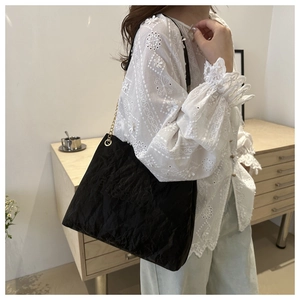 Detail of black pleated nylon tote bag featuring embossed FASHION logo and gold chain strap