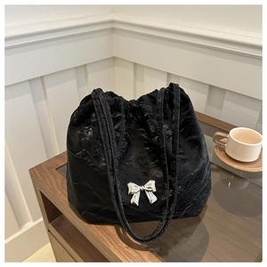 Close-up of black pleated tote bag featuring a silver bow buckle on wooden table