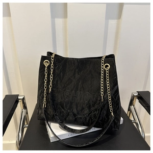 Detailed macro view of black pleated tote bag with golden chain and embossed fashion logo