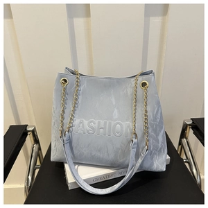 Detail of light blue tote bag with embossed Fashion text and gold chain strap