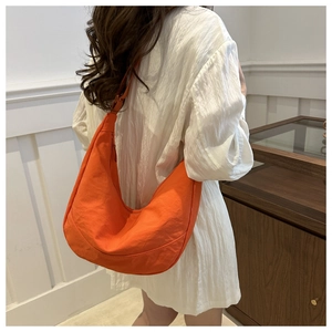 Gedetailleerd beeld van een oranje hobo-tas met nylon textuur op de schouder van een model