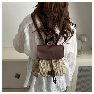 Close-up of woven straw backpack with brown leather flap and drawstring closure details