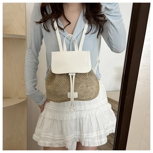Detail of woven straw backpack featuring white leather flap and drawstring closure