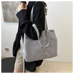 Gray canvas tote bag with dual front pockets and silver buckle, shown on a model side-view