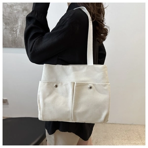 Detail of off-white canvas tote bag featuring dual front pockets and wide shoulder straps