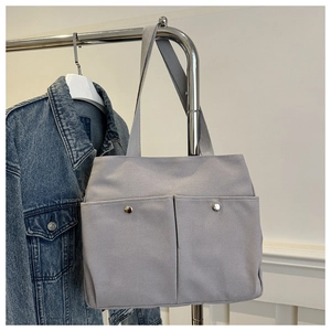 Detail of light gray canvas tote bag featuring large front pockets with metal buttons