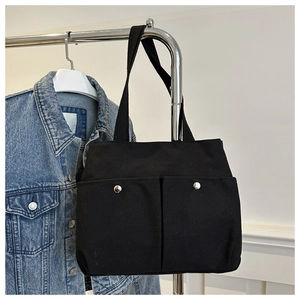 Detail of black canvas tote bag with front metal buckle pockets on a clothes hanger