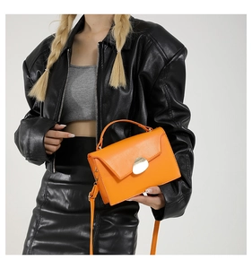 Detail of orange patent leather handbag featuring unique silver irregular buckle and top handle