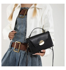 Close-up of a minimalist black flap handbag featuring a distinctive gold metal buckle