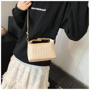 Détail d'un sac à bandoulière en paille tressée beige avec finitions en cuir marron et boucles