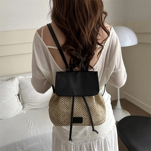 Women's straw backpack with black leather flap and drawstring in a cozy indoor setting