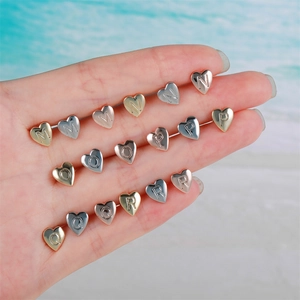 Polished heart-shaped initial stud earrings set in gold, silver, and rose gold tones