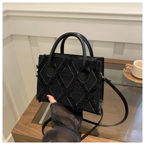 Detail of black denim handbag featuring quilted frayed edges and leather handles