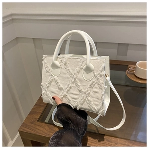 Detail of white frayed denim crossbody bag with textured rhombus pattern and gold hardware