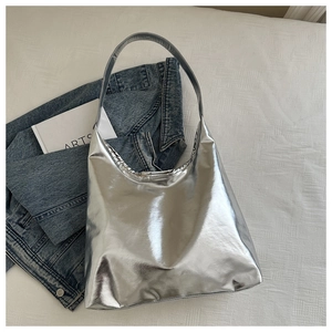 Detailed top view of a shiny silver metallic tote bag styled on white fabric
