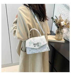 Close-up of white butterfly print crossbody bag with silver bow clasp and leather handle