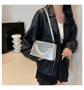 Detail of silver crocodile pattern crossbody bag with pearl handle on a black leather jacket