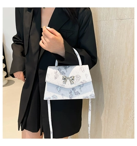 Detail of white butterfly print crossbody bag with a decorative silver bow-shaped clasp
