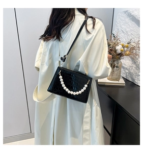 Detail shot of a black croc-embossed crossbody bag with elegant pearl chain accents