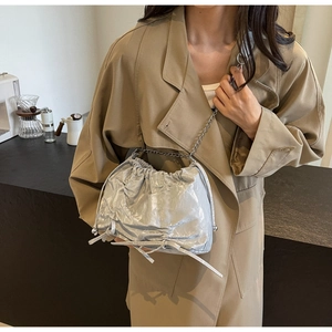Silver pleated cloud bag with metal chain strap and drawstring details on a trench coat