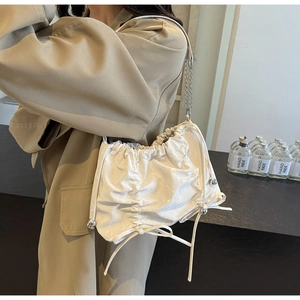 Detail of a beige pleated drawstring bag featuring soft glossy leather and silver chain