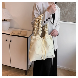 Detail view of cream drawstring bag featuring sparkling rhinestones and ruffled handles