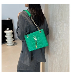 Detail der grünen Kroko-Tasche mit goldenem S-Logo und Kette an einem Modell