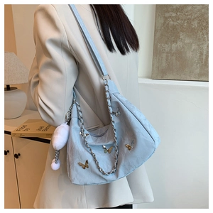 Détail du sac bandoulière bleu clair texturé avec papillons argentés et pompon blanc