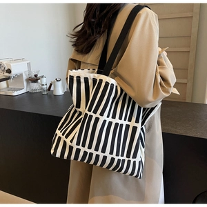 Detail of a large canvas tote bag with black stripes worn over a tan trench coat