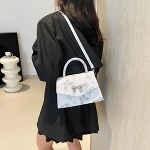 White butterfly print handbag with silver bow buckle worn over the shoulder by model