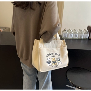 Lifestyle shot of an off-white canvas tote bag with a cartoon bear print and front pocket