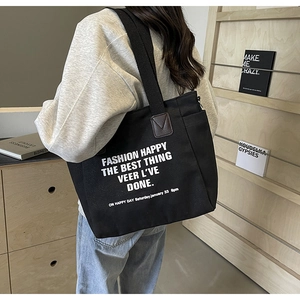 Close-up of black canvas tote bag with white lettering and brown leather strap detail