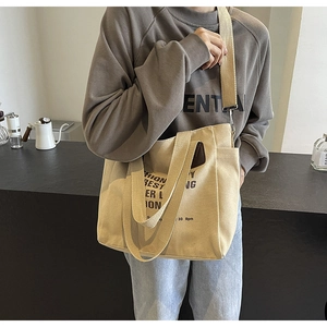 Detail of canvas tote bag showing side pocket, thick shoulder strap and black text print