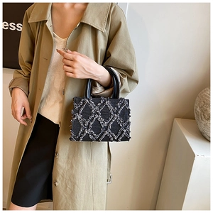 Close-up of quilted denim handbag with frayed edges and sleek black leather handles