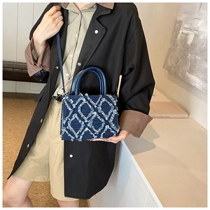 Close-up of blue denim handbag featuring distressed tassel quilted pattern and leather handle