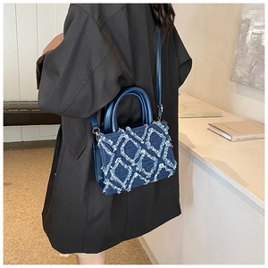 Detail of denim quilted handbag showing fringe edges and blue faux leather handle