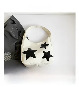 Detail view of cream canvas tote bag with black star patches and wide handle