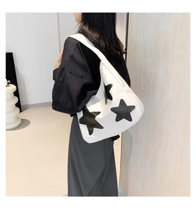 Close-up of minimalist white canvas tote bag with black star patterns and soft leather strap